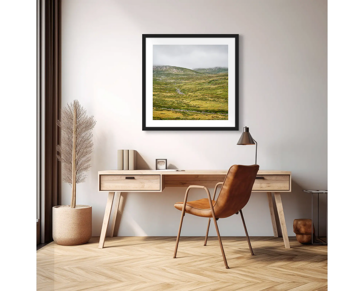 Drizzle. Framed wall art print of Snowy River, Kosciuszko National Park,  with a black frame in an apartment, above a wooden desk. 