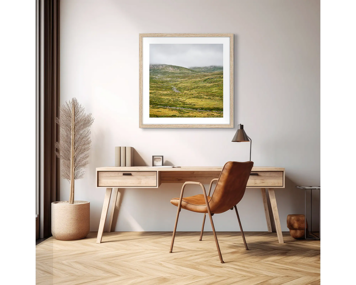 Drizzle. Framed wall art print of Snowy River, Kosciuszko National Park,  with a timber frame in an apartment, above a wooden desk. 