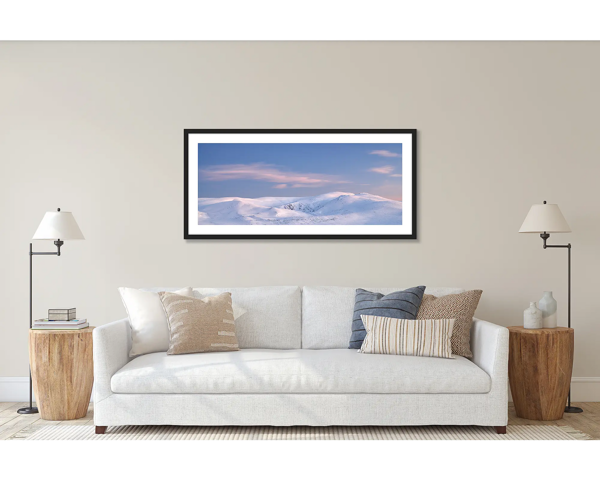 Early Morning. Wall art print of a Snowy Mountains sunrise, with a black frame, hung above a white couch.