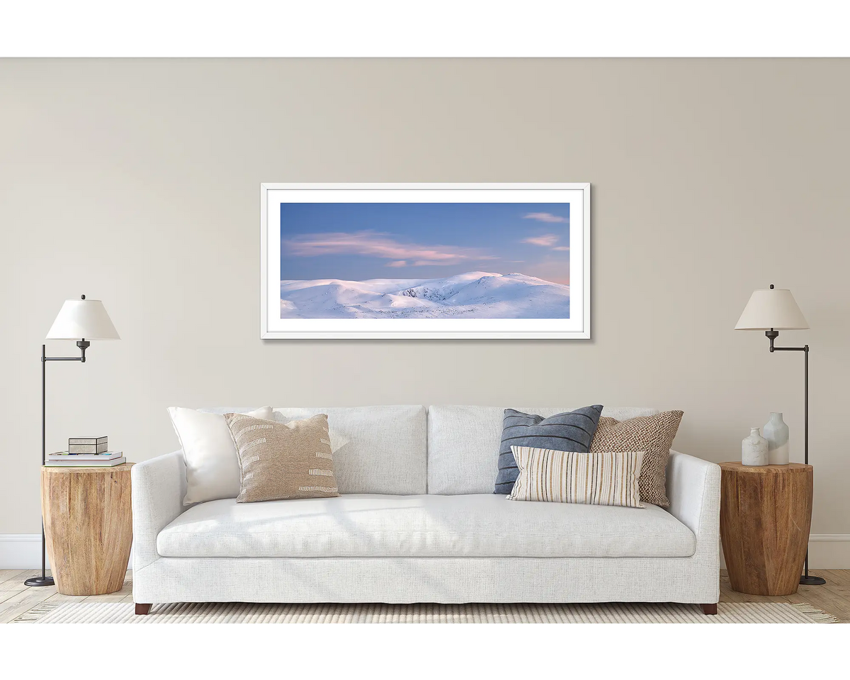 Early Morning. Wall art print of a Snowy Mountains sunrise, with a white frame, hung above a white couch.