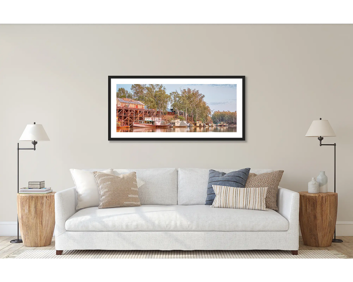 Echuca Lineup. Wall art print of wall art print of paddle steamers and Echuca Wharf, framed in a black frame, and hung above a couch. 