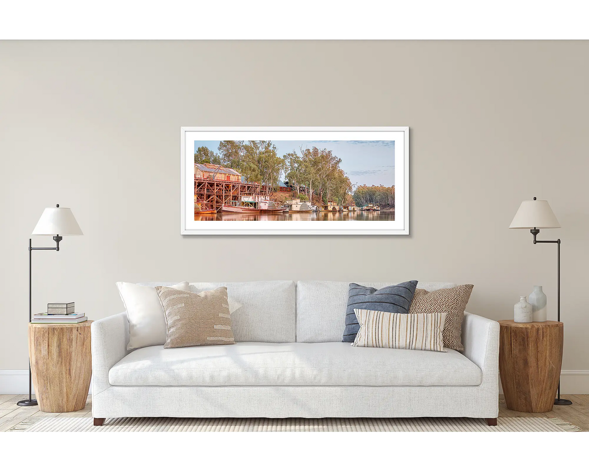 Echuca Lineup. Wall art print of wall art print of paddle steamers and Echuca Wharf, framed in a white frame, and hung above a couch. 