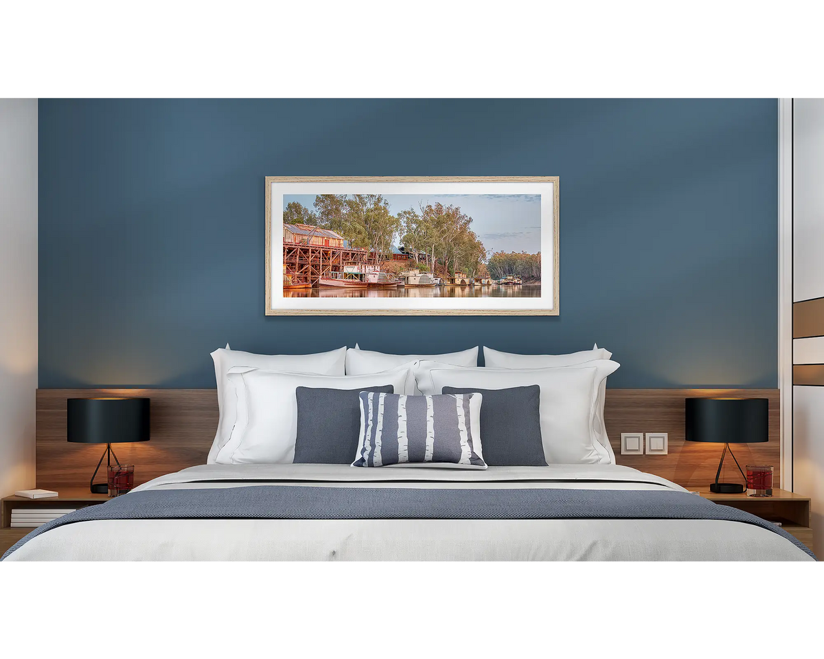 Echuca Lineup. Wall art print with a timber frame of paddle steamers and the Echuca Wharf, hung above a bed in a hotel room. 