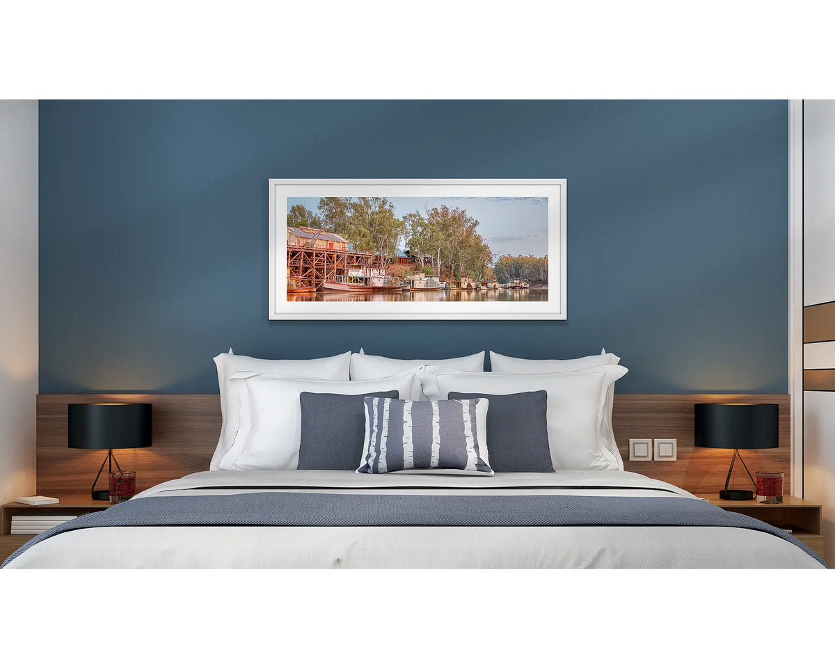 Echuca Lineup. Wall art print with a white frame of paddle steamers and the Echuca Wharf, hung above a bed in a hotel room. 