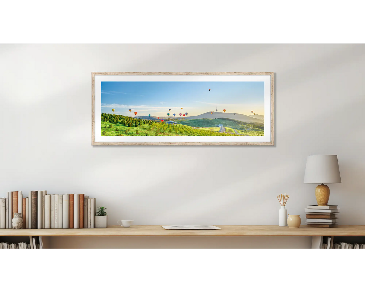 Enlighten. Wall art print of hot air balloons over the arboretum at sunrise, framed with a timber frame and hung above a small desk. 