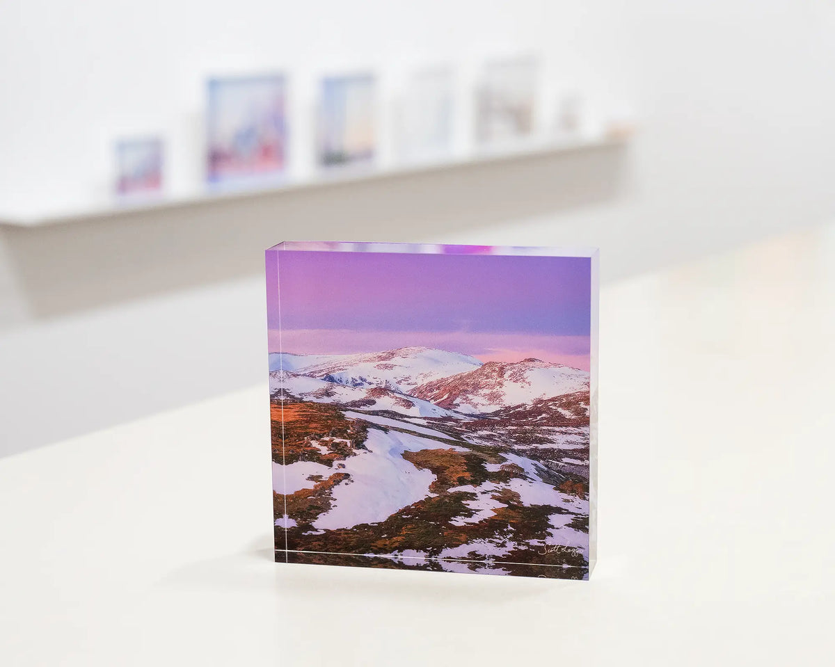 Escape To The Mountains. Acrylic block of sunset over Kosciuszko National Park, in gallery with display shelf behind.