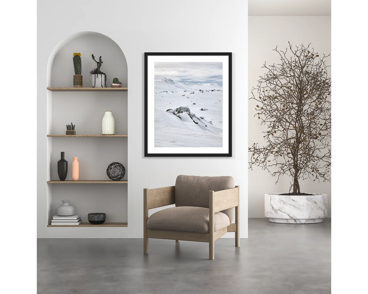 Etheridge Lines. Snowy Mountains wall art print with a black frame, hung above a chair.