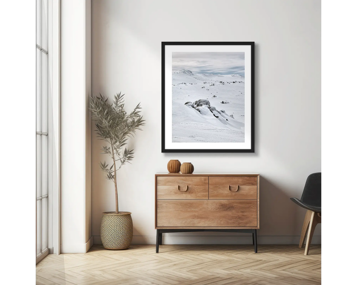 Etheridge Lines. Snowy Mountains wall art print with a black frame, hung on an apartment wall above a side table.