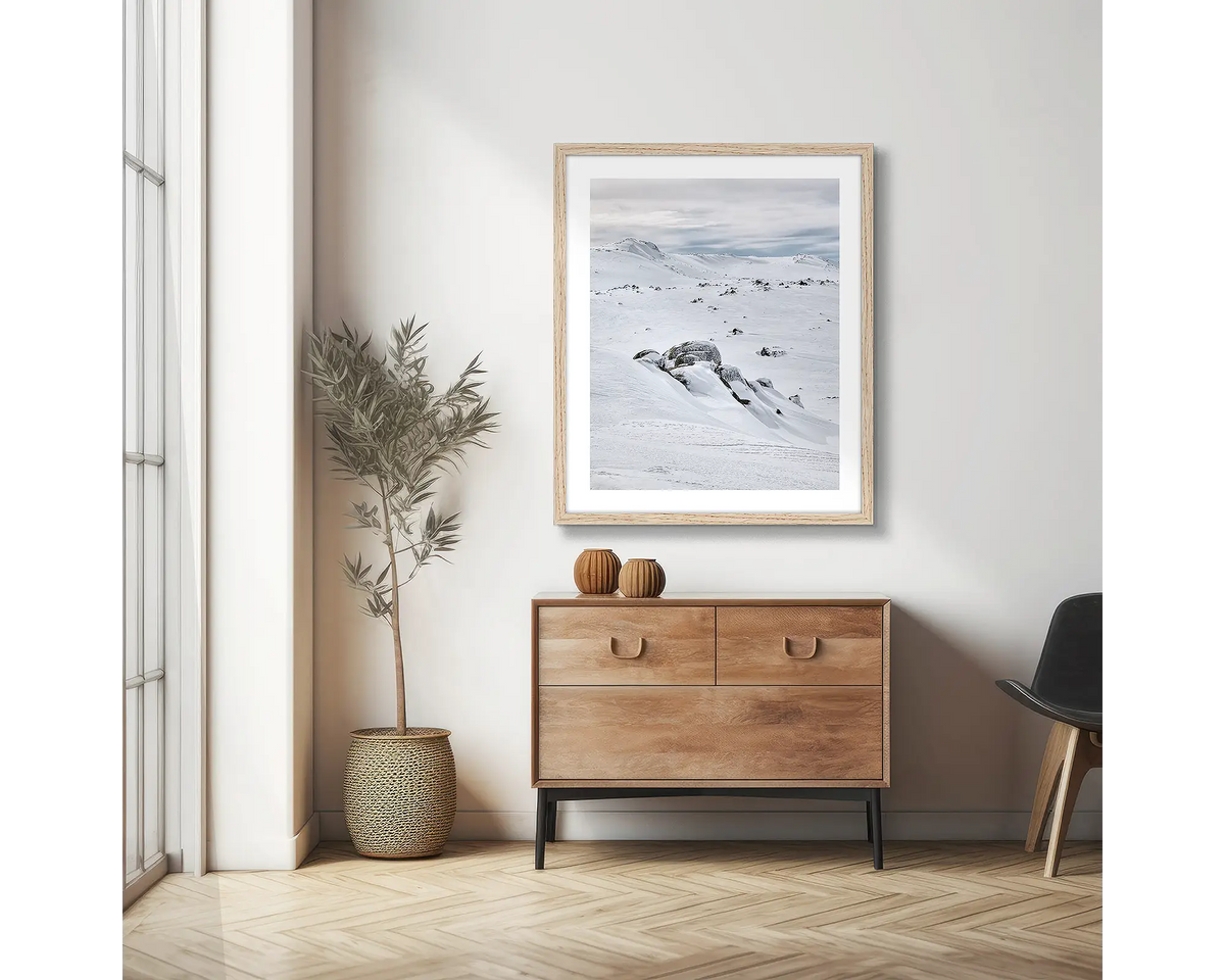 Etheridge Lines. Snowy Mountains wall art print with a timber frame, hung on an apartment wall above a side table.