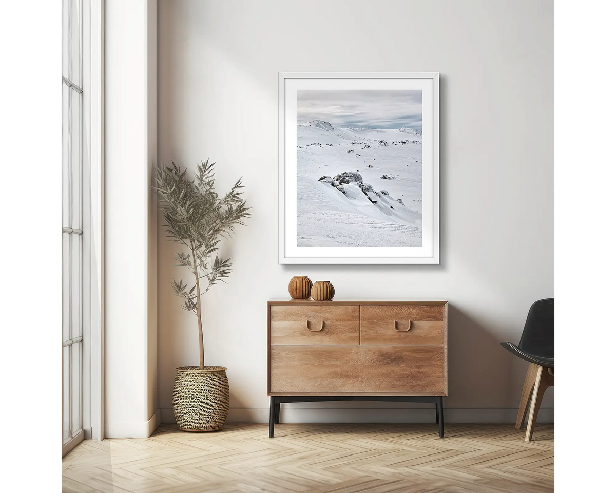 Etheridge Lines. Snowy Mountains wall art print with a white frame, hung on an apartment wall above a side table.