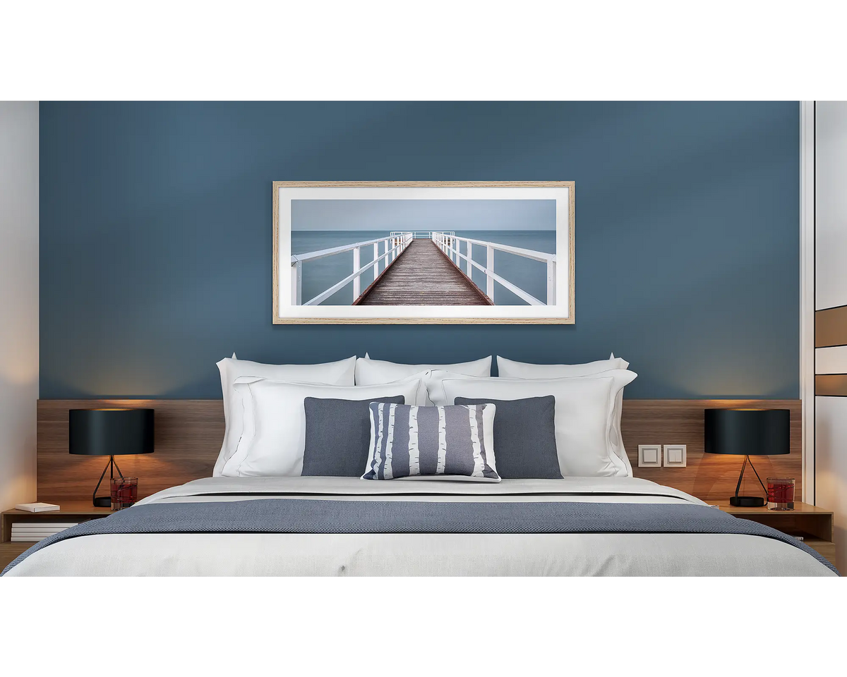 Evening Calm. Framed wall art print of a jetty with a timber frame, hung above a bed in a hotel room. 