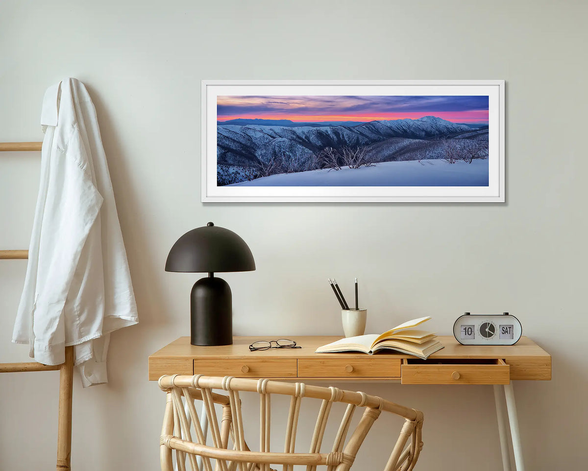 Evening Glory. Winter snow sunrise wall art print with white frame, above a small table.