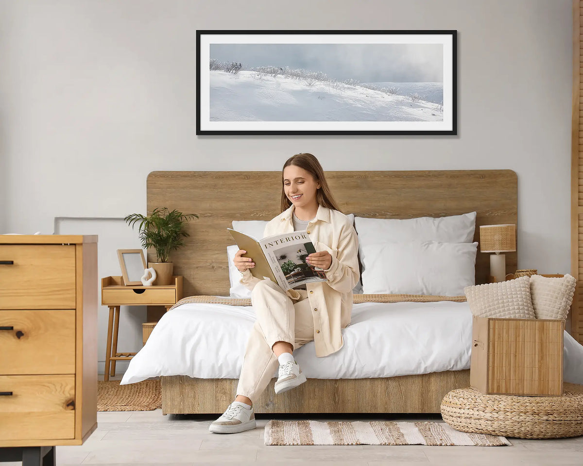 Exposed. Tasmanian wall art print, with a black frame hung above a bed, with a woman reading a magazine. 