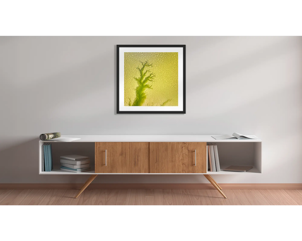 Extend. Aerial abstract framed wall art print, with a black frame, hung above a side table. 