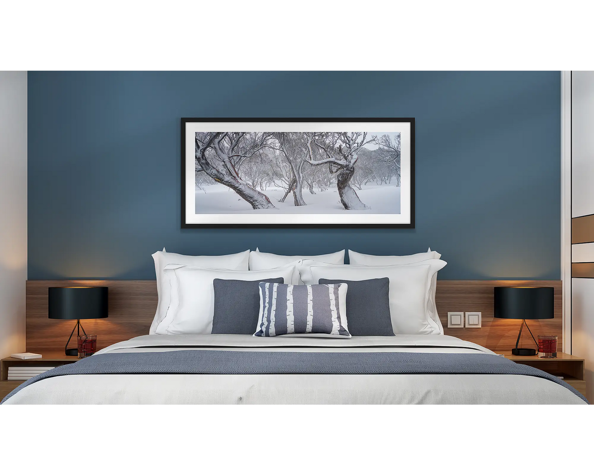 Family Twist. Old twisted snow gums in snow, wall art print in a black frame hung above a bed in a hotel room. 
