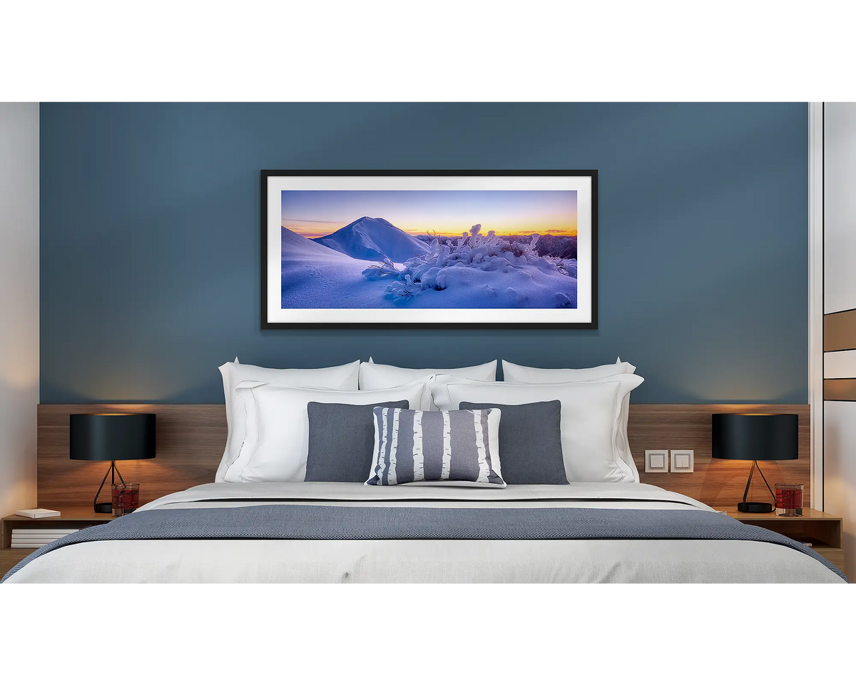 Feathertop Dawn. Wall art print of a winter sunrise over Mount Feathertop, framed with a black frame and hung above a bed in a hotel room.