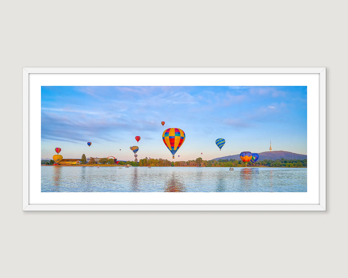 Framed photograph of hot air balloons floating over a lake with mountains in the background.