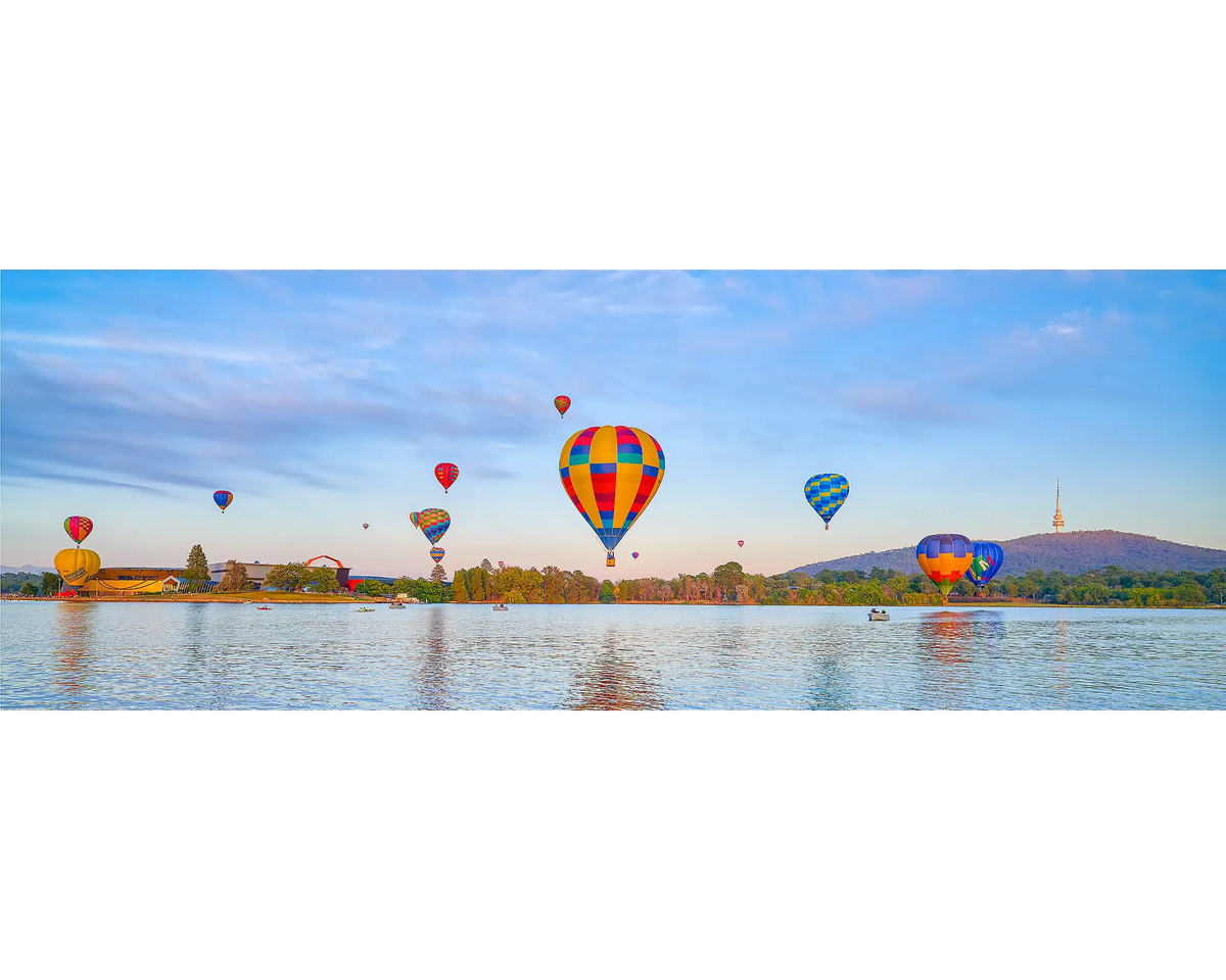 Colourful hot air balloons over a Lake Burley Griffin with Black Mountain in the background.