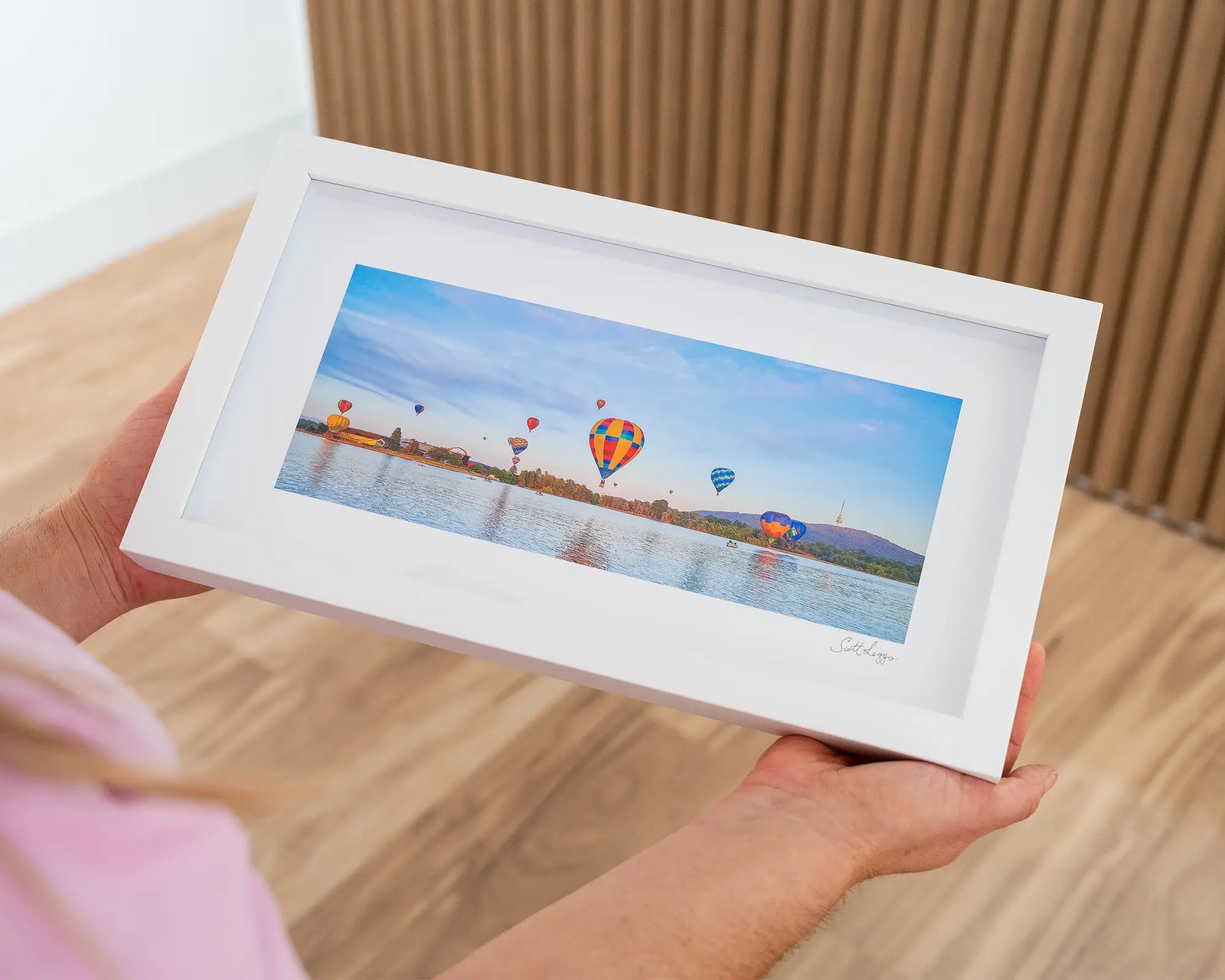 Framed photograph of hot air balloons floating over a lake with mountains in the background.