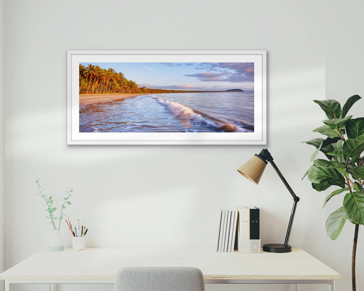 Four Mile Sunrise. Framed wall art print of Four Mile Beach, Port Douglas, with a white frame hung above a home office desk. 