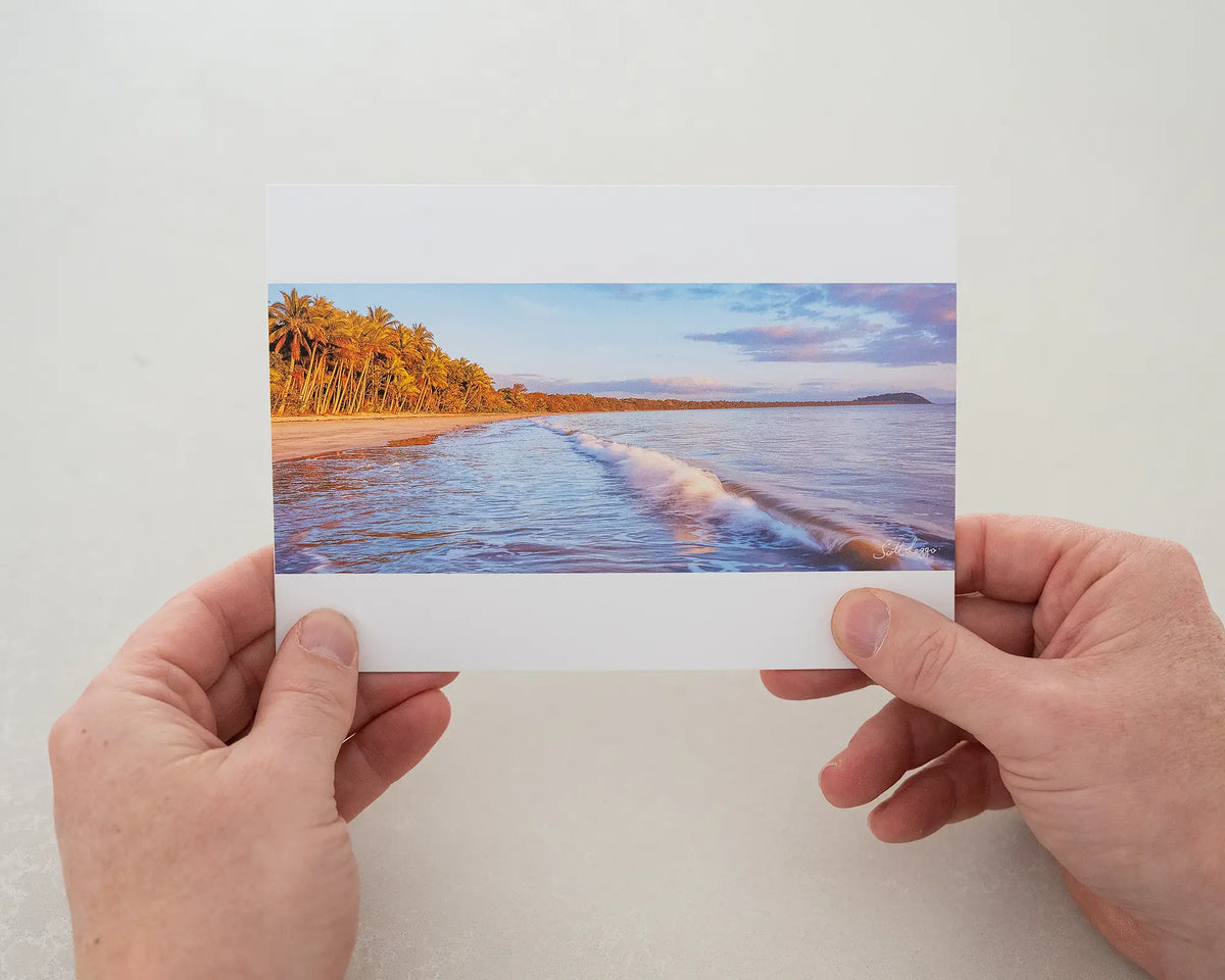 Four Mile Sunrise greeting card of sunrise over Four Mile Beach, Port Douglas, being held in two hands.
