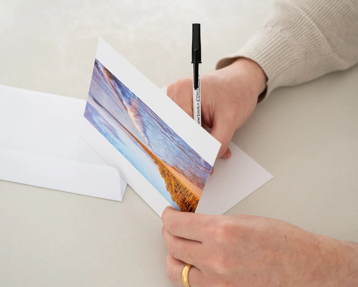 Four Mile Sunrise greeting card of sunrise over Four Mile Beach, Port Douglas, being written in with black pen.