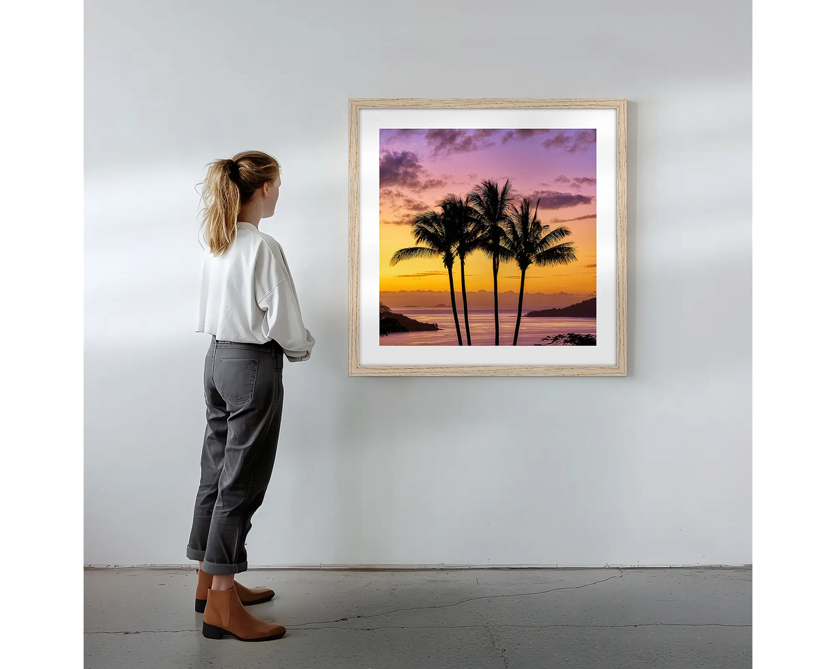 Getaway.  Wall art print with timber frame featuring Hamilton Island palm trees, hung on a wall with woman admiring.