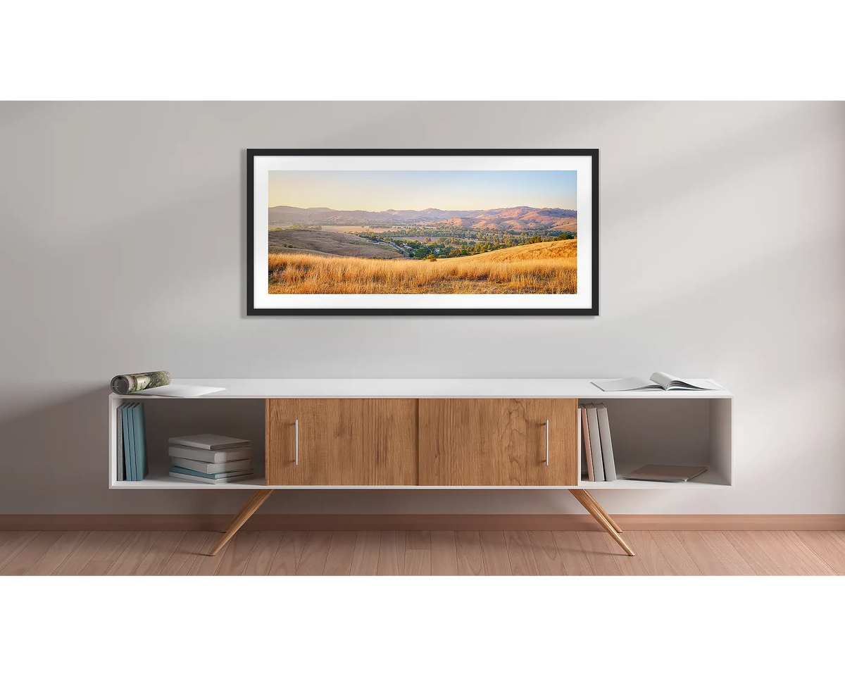 Golden Riverina. Wall art print with a black frame, of a sunrise over Gundagai, hung above a side table. 