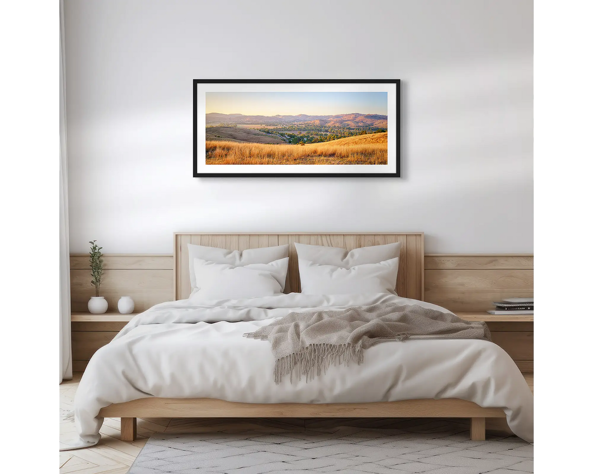 Golden Riverina. Wall art print with a black frame, of a sunrise over Gundagai, hung above a wooden bed. 