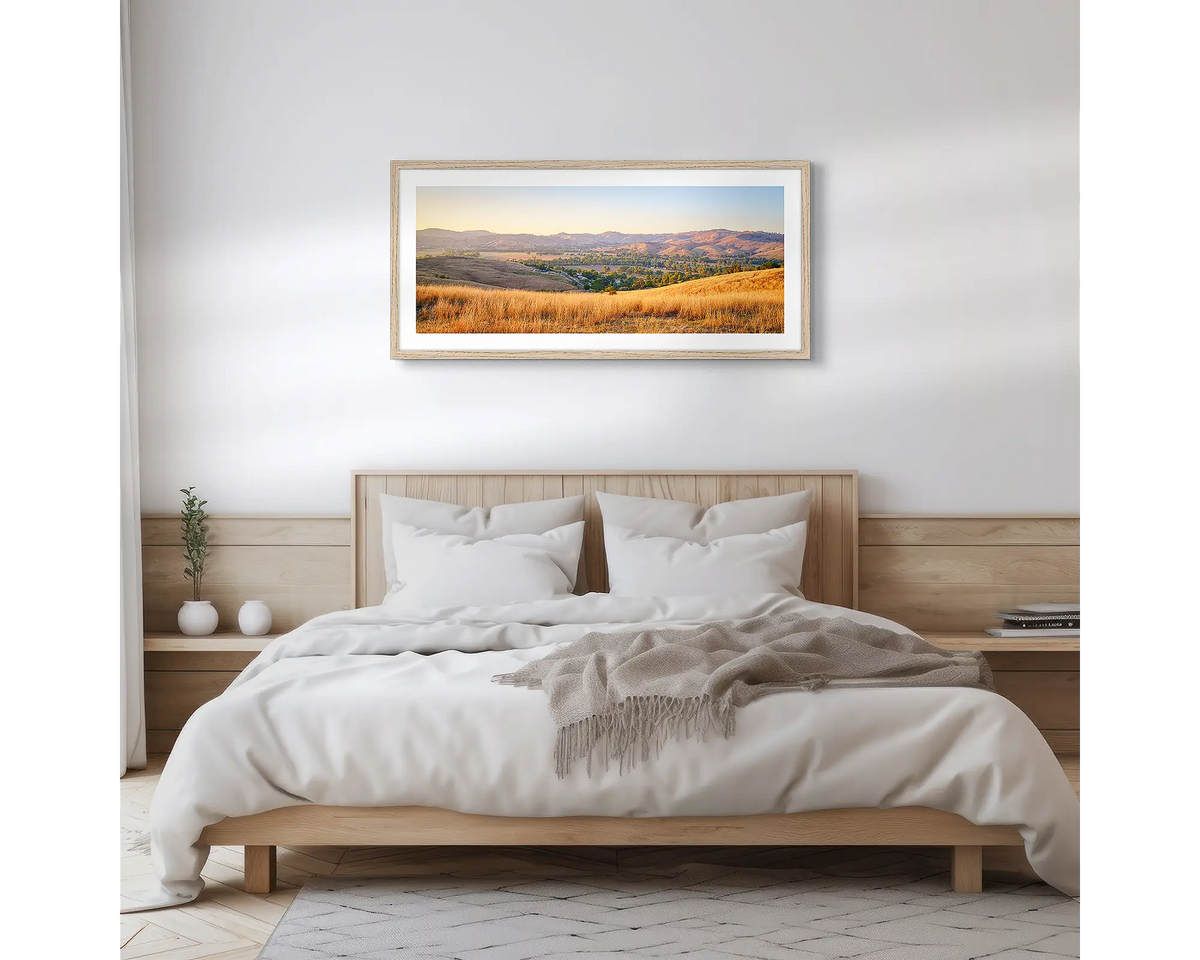 Golden Riverina. Wall art print with a Tasmanian Oak frame, of a sunrise over Gundagai, hung above a wooden bed. 