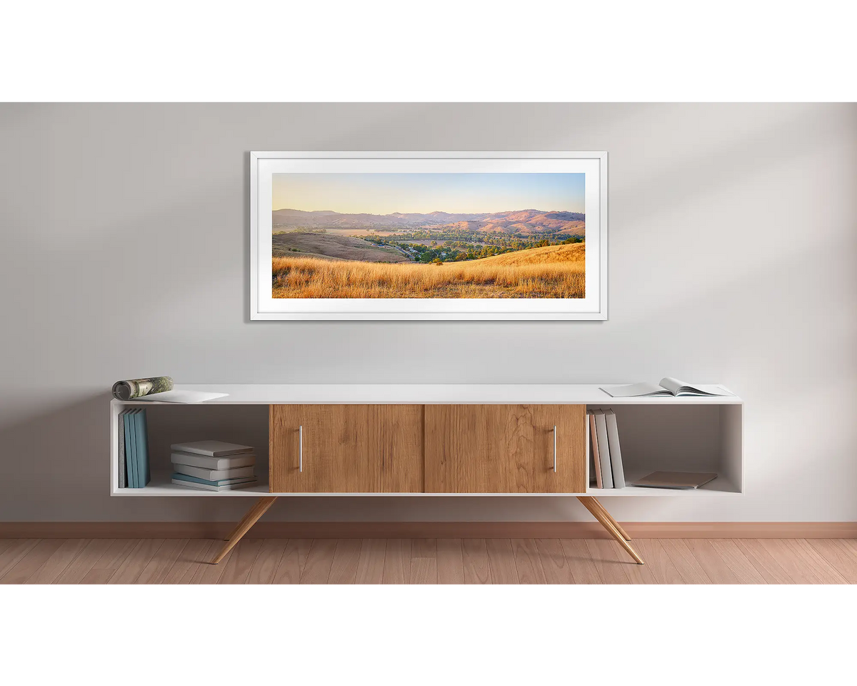 Golden Riverina. Wall art print with a white frame, of a sunrise over Gundagai, hung above a side table. 