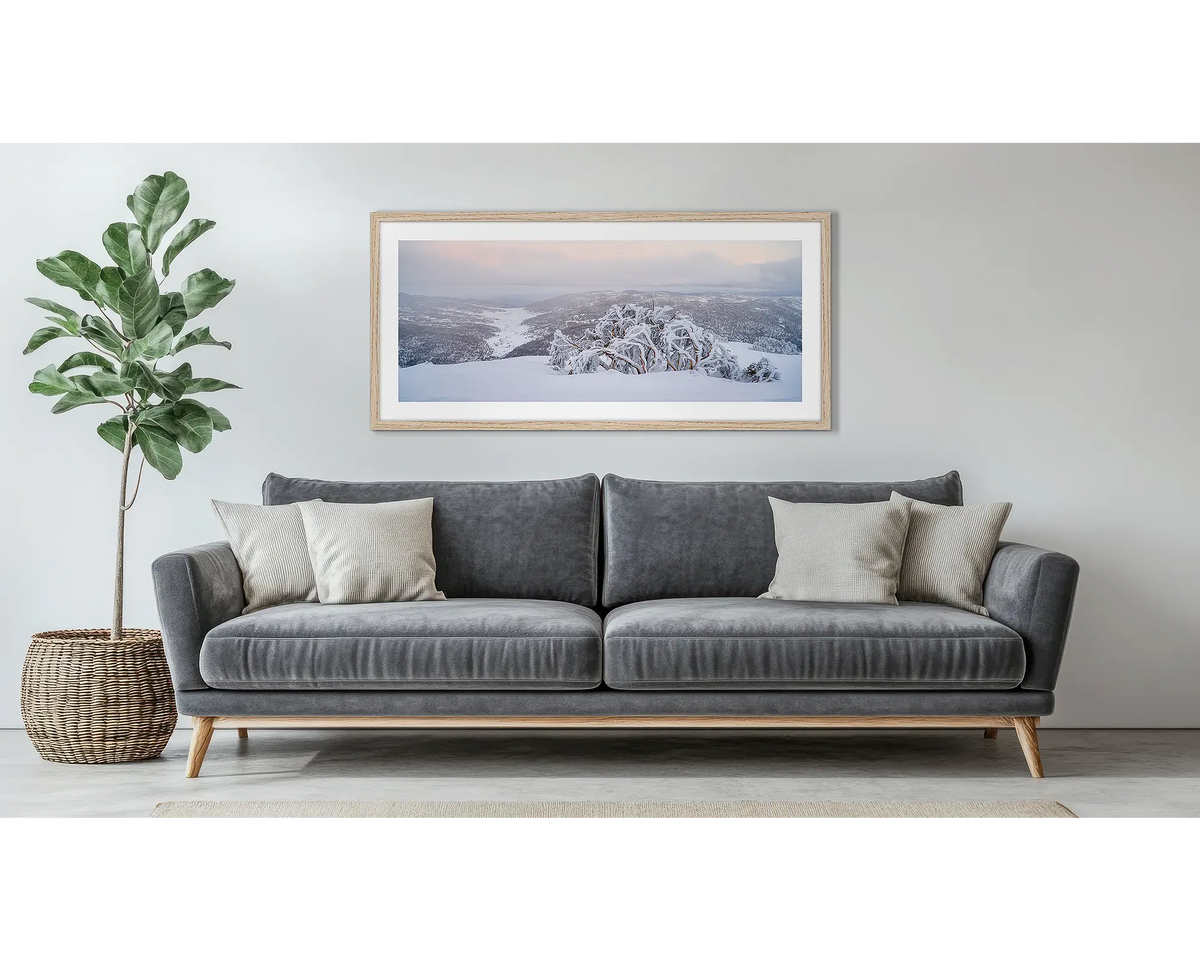 Guardian of the Valley. Wall art print of a snow gum overlooking a snow covered valley, framed in a timber frame and hung above a couch. 