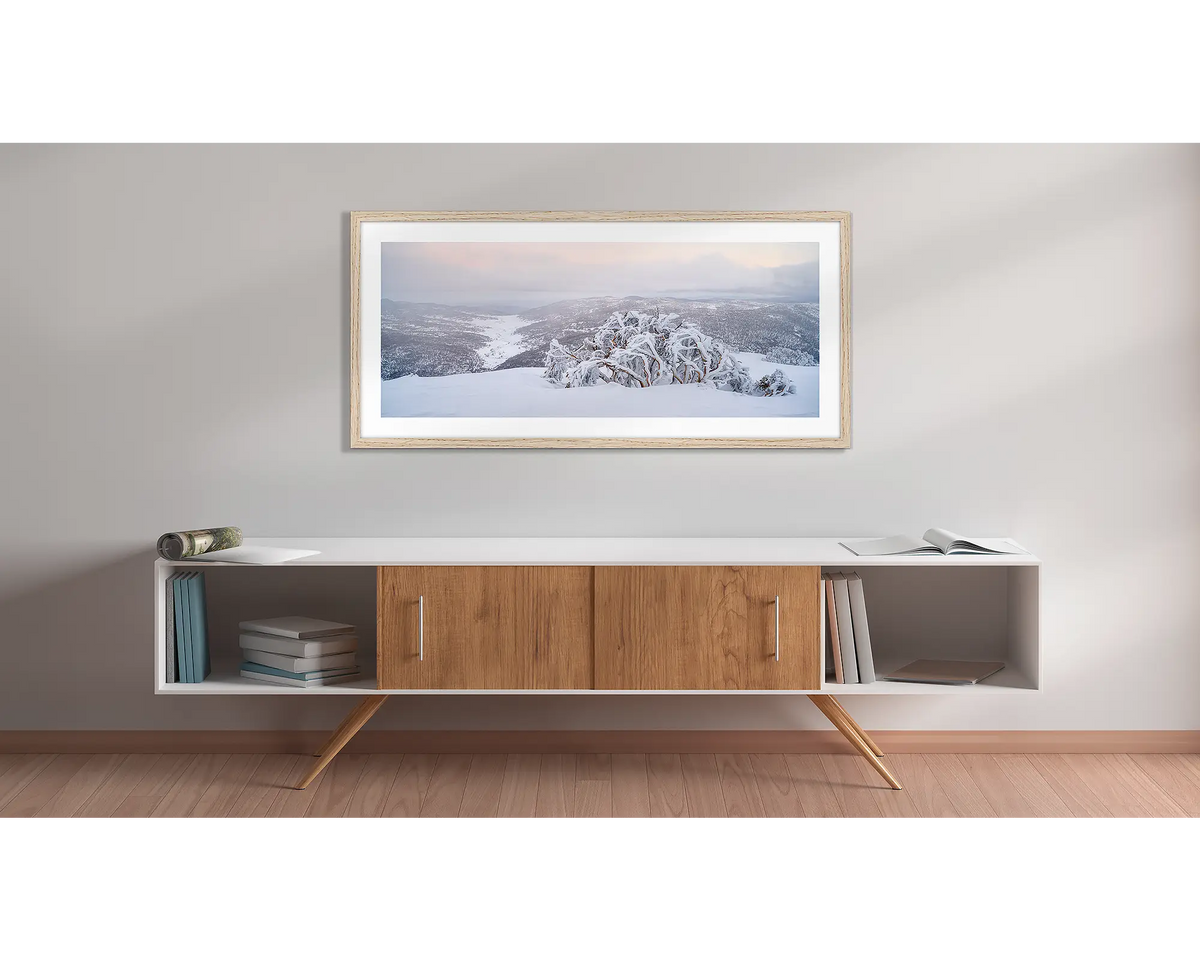 Guardian of the Valley. Wall art print of a snow gum overlooking a snow covered valley, framed in a timber frame and hung above a side table. 