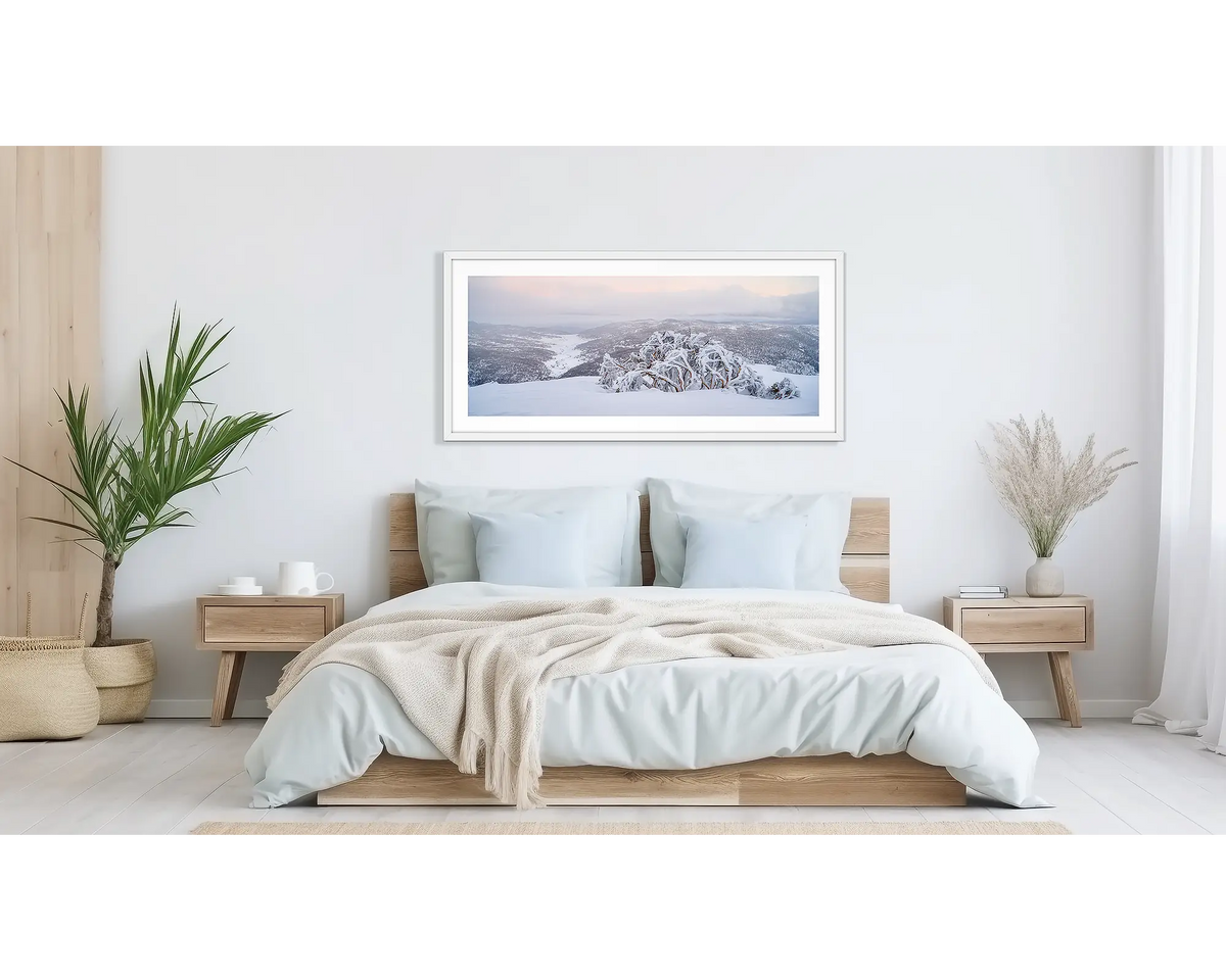Guardian of the Valley. Wall art print of a snow gum overlooking a snow covered valley, framed in a white frame and hung above a bed.