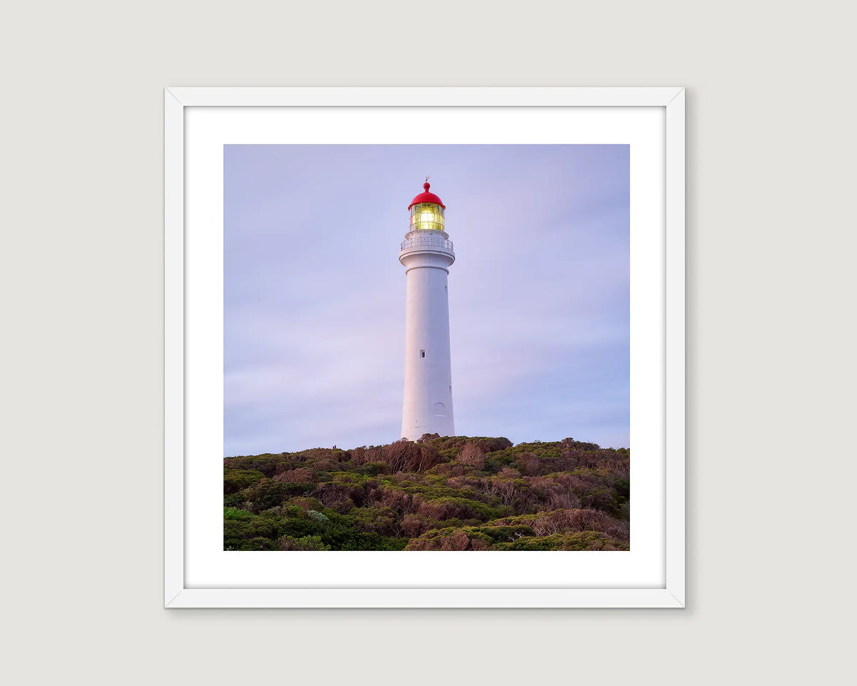 Framed wall art print of Split Point Lighthouse on a cliff surrounded by native coastal bush. 