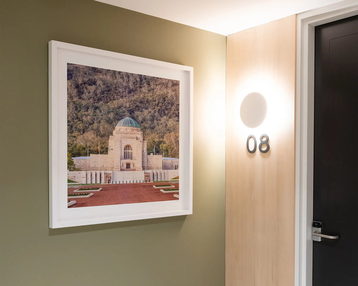 Honouring Their Spirit. Australian War Memorial, with white frame, hung on green wall in apartment building.