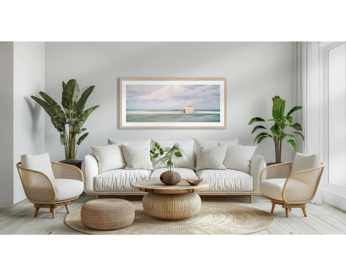 Hues of Merewether. Wall art print with a Tasmanian Oak frame, of the pumphouse, Merewether Baths, Newcastle, hung above a couch, in a lounge room. 