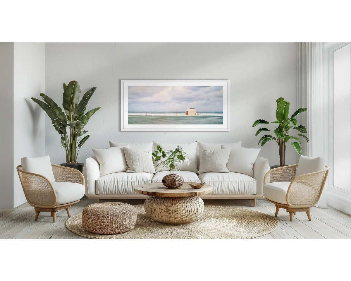 Hues of Merewether. Wall art print with a white frame, of the pumphouse, Merewether Baths, Newcastle, hung above a couch, in a lounge room. 