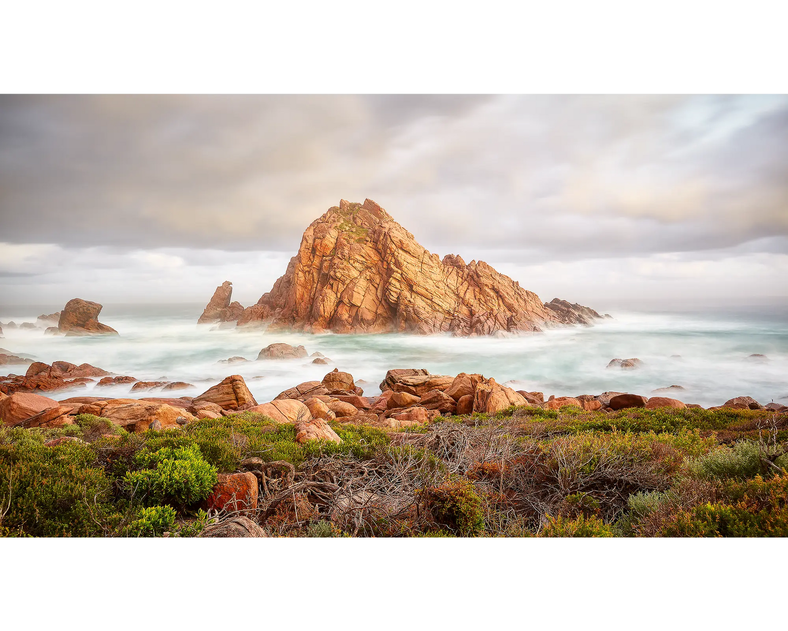 Framed photograph of a rock formation in the ocean with mist and clouds.