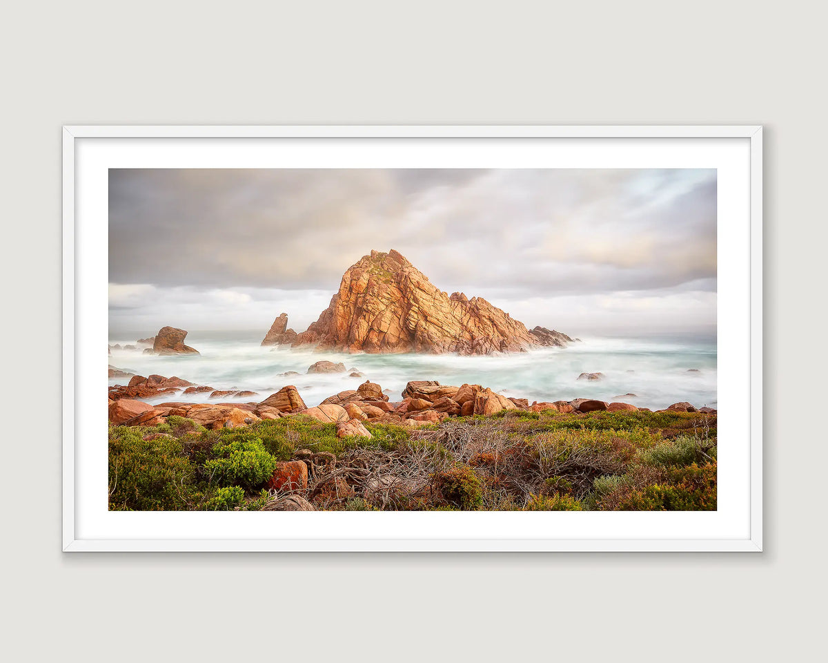 Framed photograph of a rock formation in the ocean with mist and clouds.