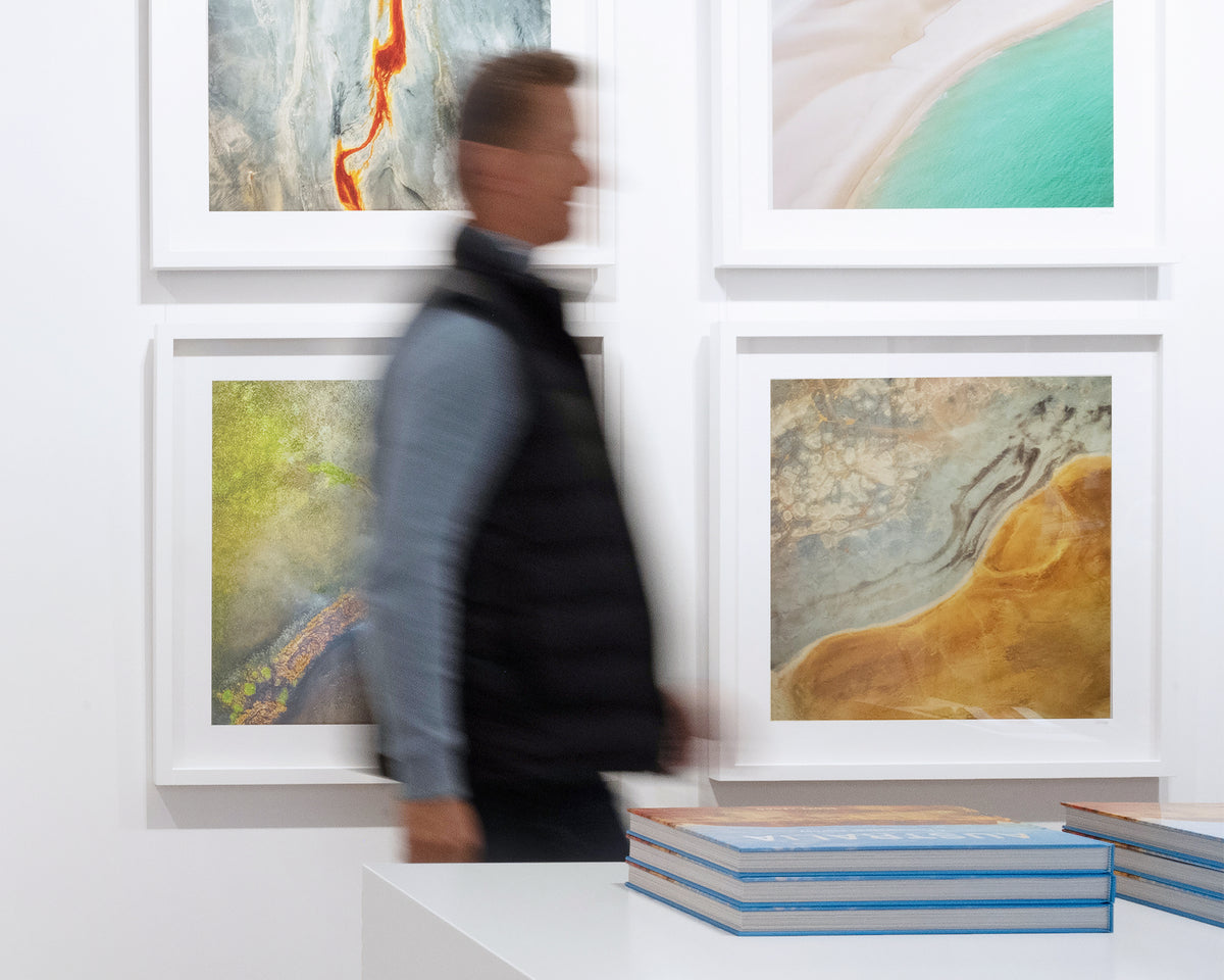 Interchange. Aerial abstract artwork of a dried dam New South Wales, in gallery with person walking past and books in foreground.
