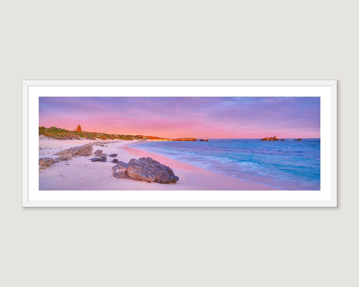 Framed coastal wall art print of a vibrant sunrise reflecting on white sand and aqua water at Pinkys Beach. 