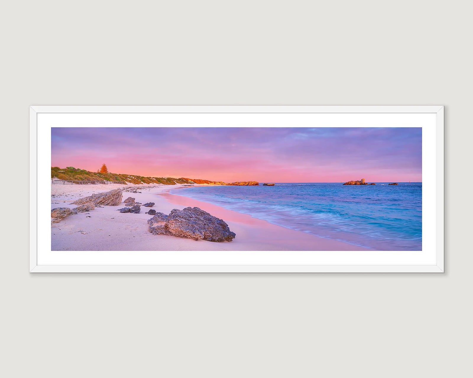 Framed coastal wall art print of a vibrant sunrise reflecting on white sand and aqua water at Pinkys Beach. 
