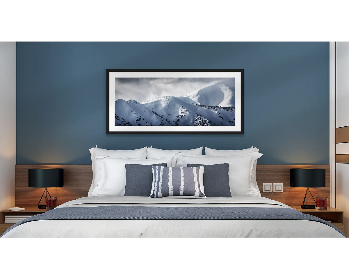 Journey to the Summit. Wall art print of Mount Feathertop with snow, framed with a black frame and hung above a bed.