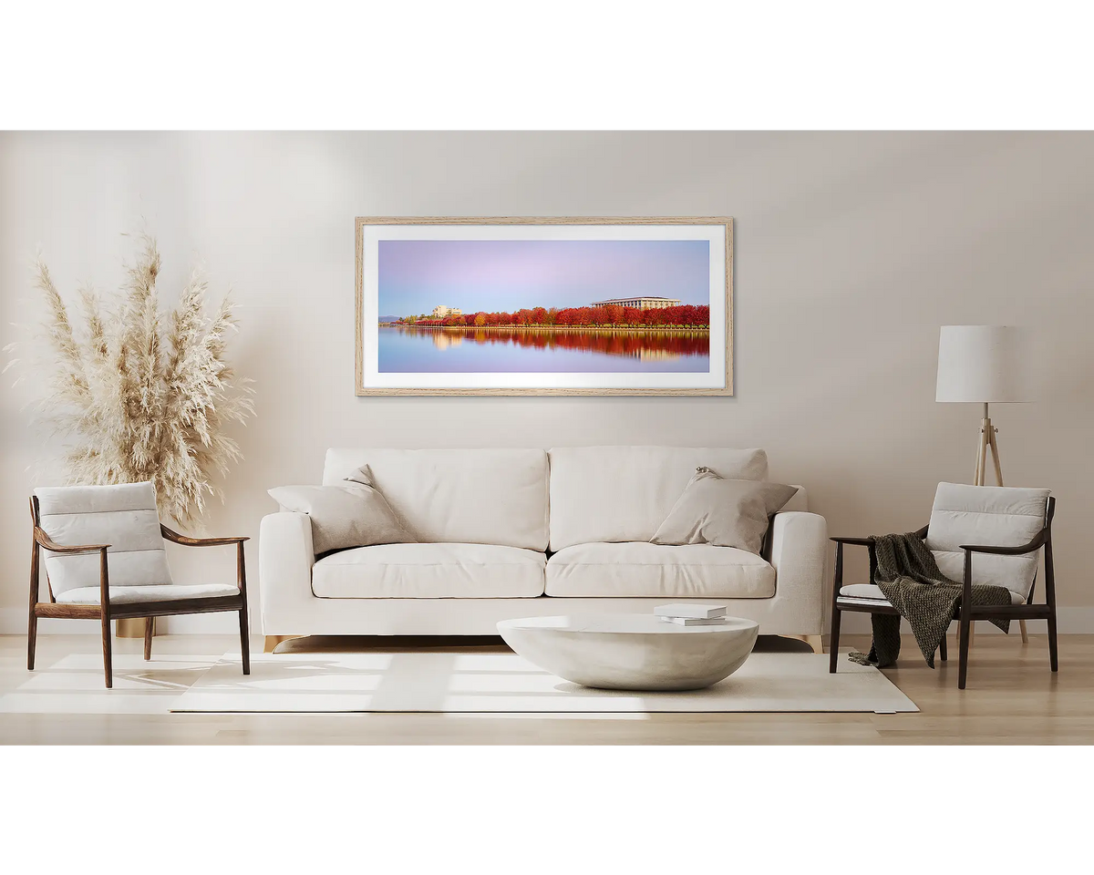 Lakeside Hues. Wall art print with timber frame of red autumn trees beside Lake Burley Griffin, hung above a couch.