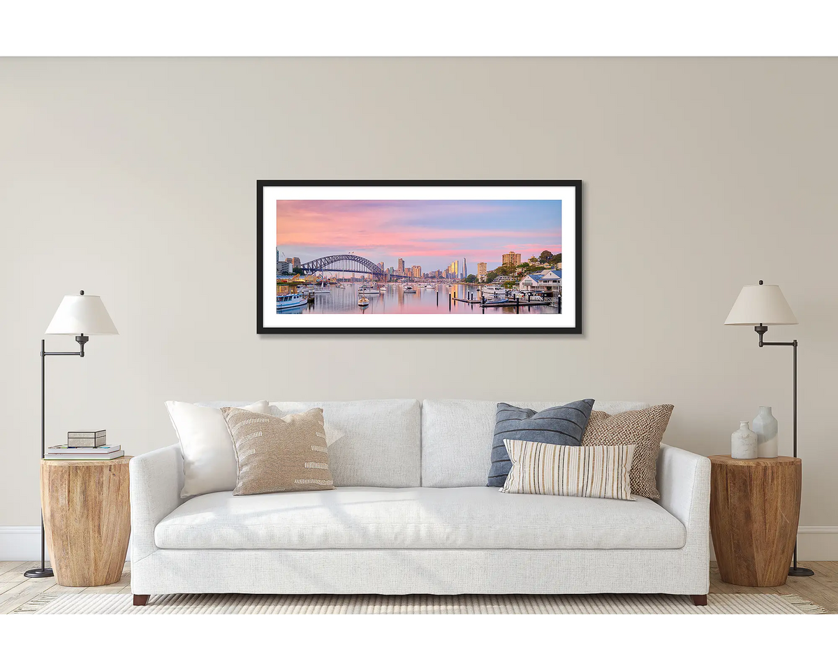 Lavender Sunrise. Wall art print of a sunrise over Lavender Bay, Sydney, framed in a black frame and hung above a couch. 