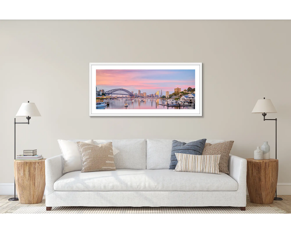 Lavender Sunrise. Wall art print of a sunrise over Lavender Bay, Sydney, framed in a white frame and hung above a couch. 