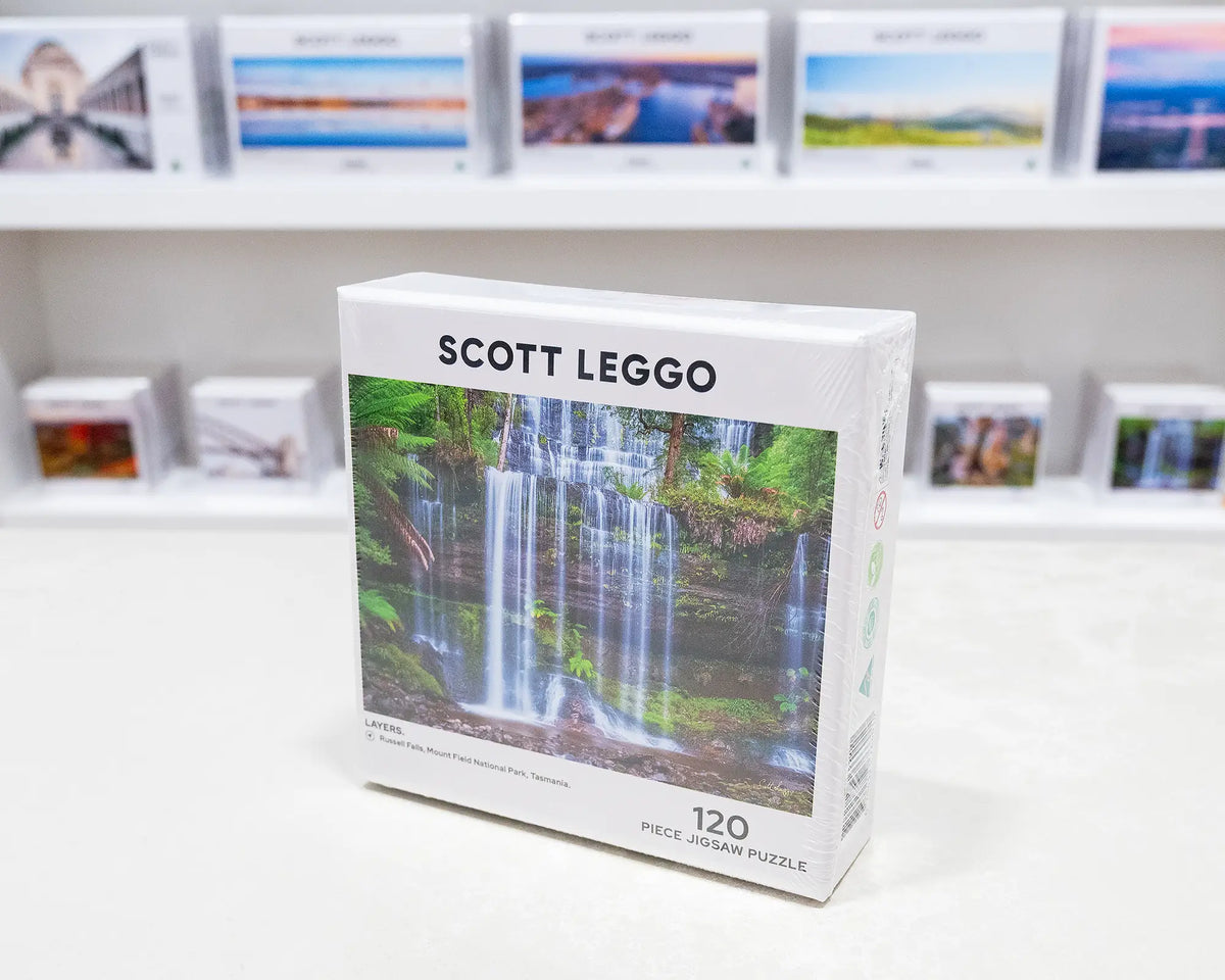 Layers. 120 piece jigsaw puzzle of Russell Falls, Tasmania, on gallery desk with more puzzles in background.