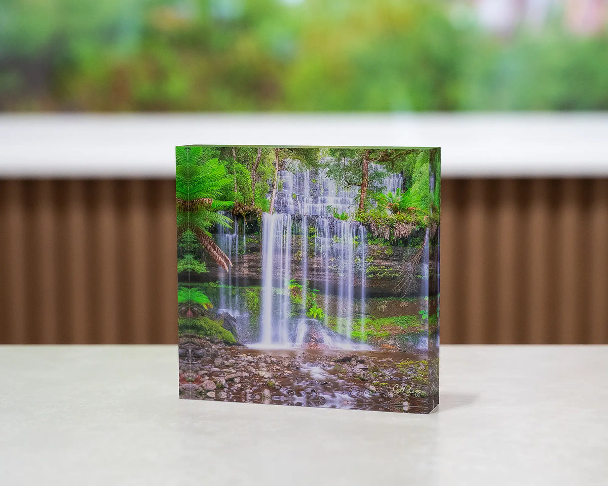 Layers. Acrylic block Russell Falls, Mount Field National Park, Tasmania, on desk with large artwork in background.