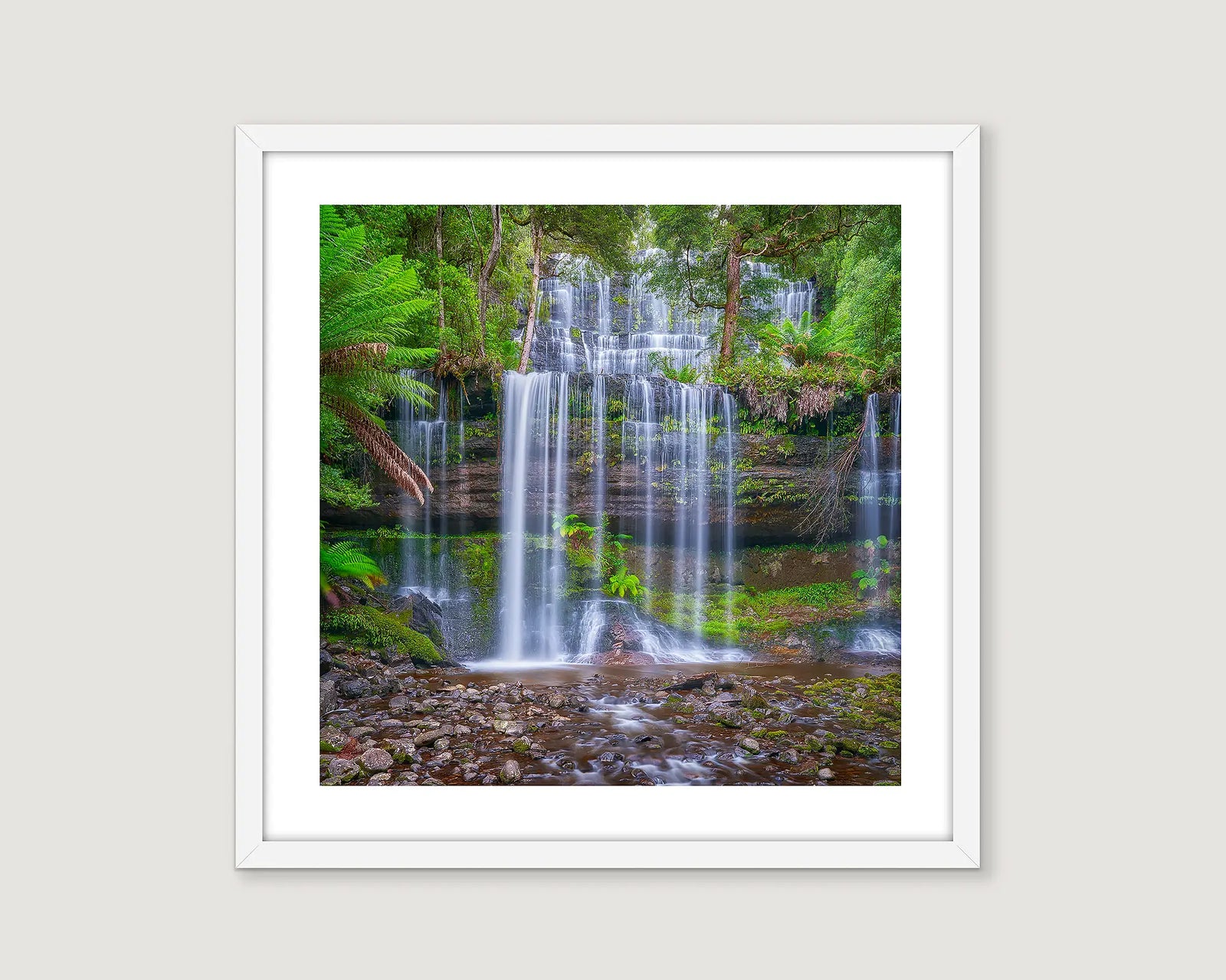 Framed photographic print of Russell Falls flowing with water over layers of rocks with rainforest plants.